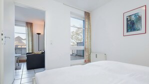 A modern hotel room with a large bed, a view through a window, and a painting on the wall. - Dünenblick Wohnung 50 (Ostseebad Boltenhagen)