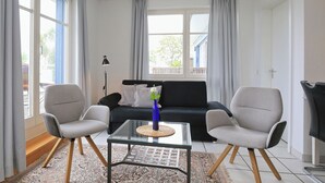 A living room with a sofa, two armchairs, a glass coffee table, and a lamp. - Dünenblick Wohnung 50 (Ostseebad Boltenhagen)