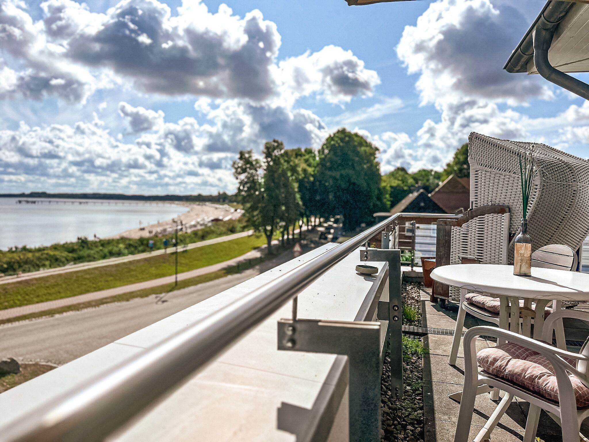 En balkon med udsigt til en strand og en vej. Der er et bord og stole på balkonen.