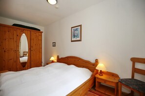 A bedroom with a wooden bed, two bedside tables with lamps, a wooden wardrobe, and a framed picture on the wall. - Sünnslag Wohnung 080 (Ostseebad Boltenhagen)