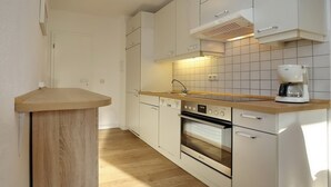 Une cuisine avec des meubles blancs, un plan de travail en bois, un four encastré et une machine à café.