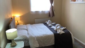 Een hotelkamer met een bed, een bedlamp, een radiator en een raam met gordijnen.