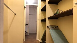 Een smalle gang met een houten vloer, een witte deur aan het einde en een klein fitmatje aan de rechterkant.