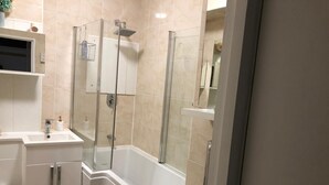 Een moderne badkamer met een douchecabine van glas, een witte wastafel en een toilet.
