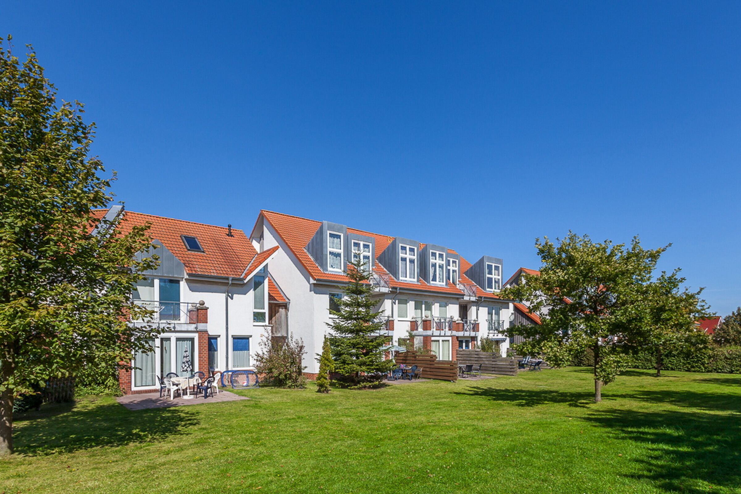 Una hilera de casas modernas con tejados rojos, un césped bien cuidado y un cielo azul despejado.
