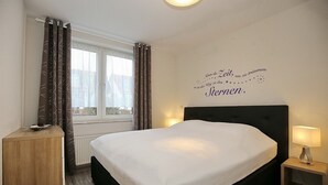 Un dormitorio con cama, una mesita de noche con lámpara, una ventana con cortinas y un adorno en la pared.