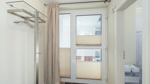 Une pièce dotée d’une porte-fenêtre coulissante, d’une étagère en verre, d’un tapis marron foncé et d’un meuble de rangement blanc avec des tiroirs.