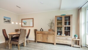 Un coin repas avec une table et des chaises en bois, un meuble avec des portes en verre et une petite plante posée sur un support.
