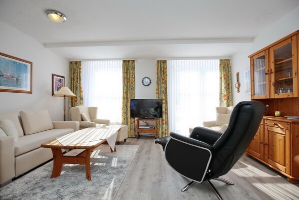 A living room with a sofa, a coffee table, a black leather chair, a television, and a wooden cabinet. - Die Ferienwohnung Nr (Ostseebad Boltenhagen)