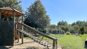 Un parque infantil con pared de escalar, columpios y zona de juegos cubierta.
