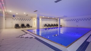 Una piscina interna con pareti piastrellate, pavimento azzurro e diverse poltrone a bordo vasca.