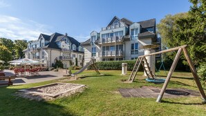 Un edificio residenziale con un'area giochi, comprensiva di scivolo e altalene, e un patio con posti a sedere all'aperto.