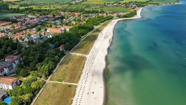 Vista aerea di una cittadina costiera con una lunga spiaggia sabbiosa, edifici residenziali e una limpida vista sul mare.