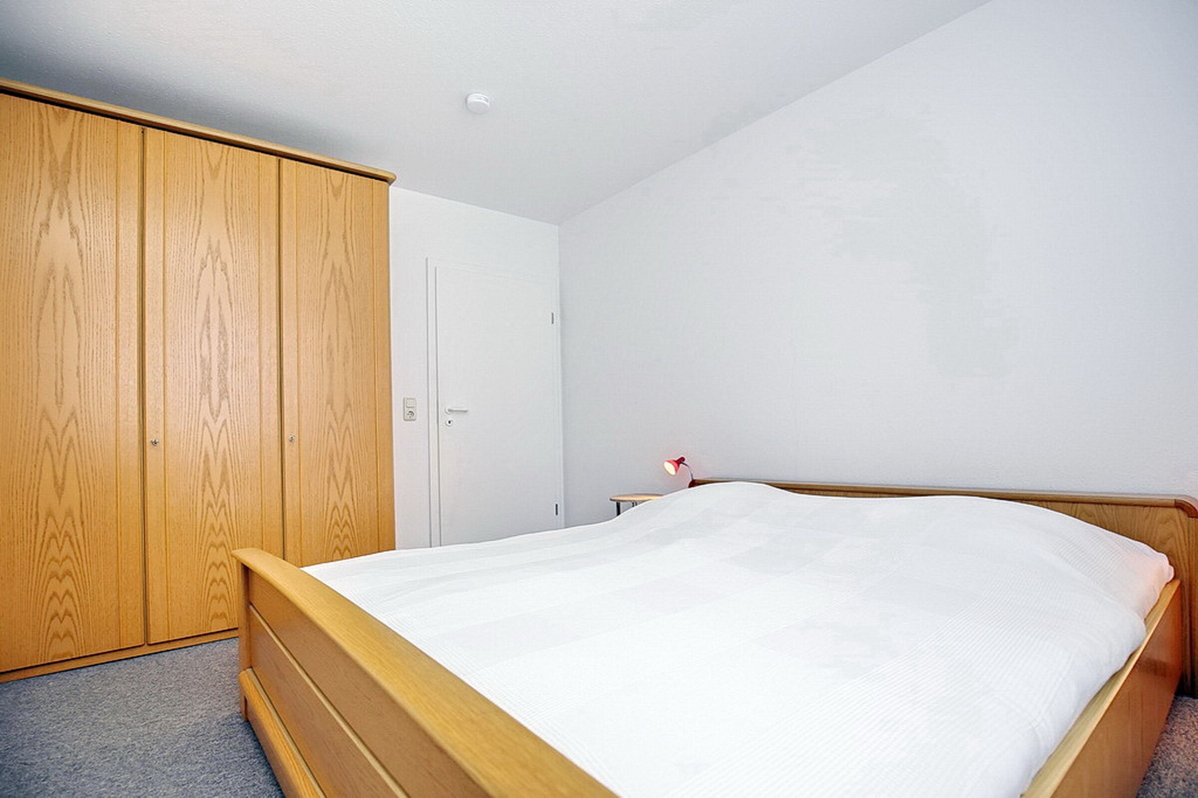 A bedroom with a wooden bed, a wardrobe, and a nightstand with a lamp.