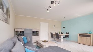 En moderne stue med en grå sofa, et træbord og et spiseområde med bord og stole.