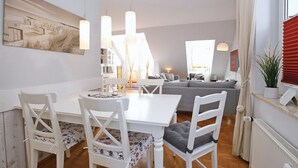 Una sala de estar moderna con un sofá blanco, una mesa de comedor con sillas blancas y un cuadro grande en la pared.