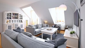 Un moderno apartamento tipo loft con techo alto, una estantería empotrada, un sofá gris, una mesa de centro blanca y un ventanal que proporciona luz natural.