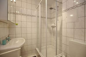 Ein Badezimmer mit einer Duschkabine, einem weißen Waschbecken und einer blauen Tasse sowie einer Toilette.