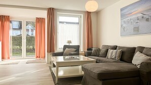 Een moderne woonkamer met een hoekbank, een glazen salontafel en een groot raam met gordijnen.
