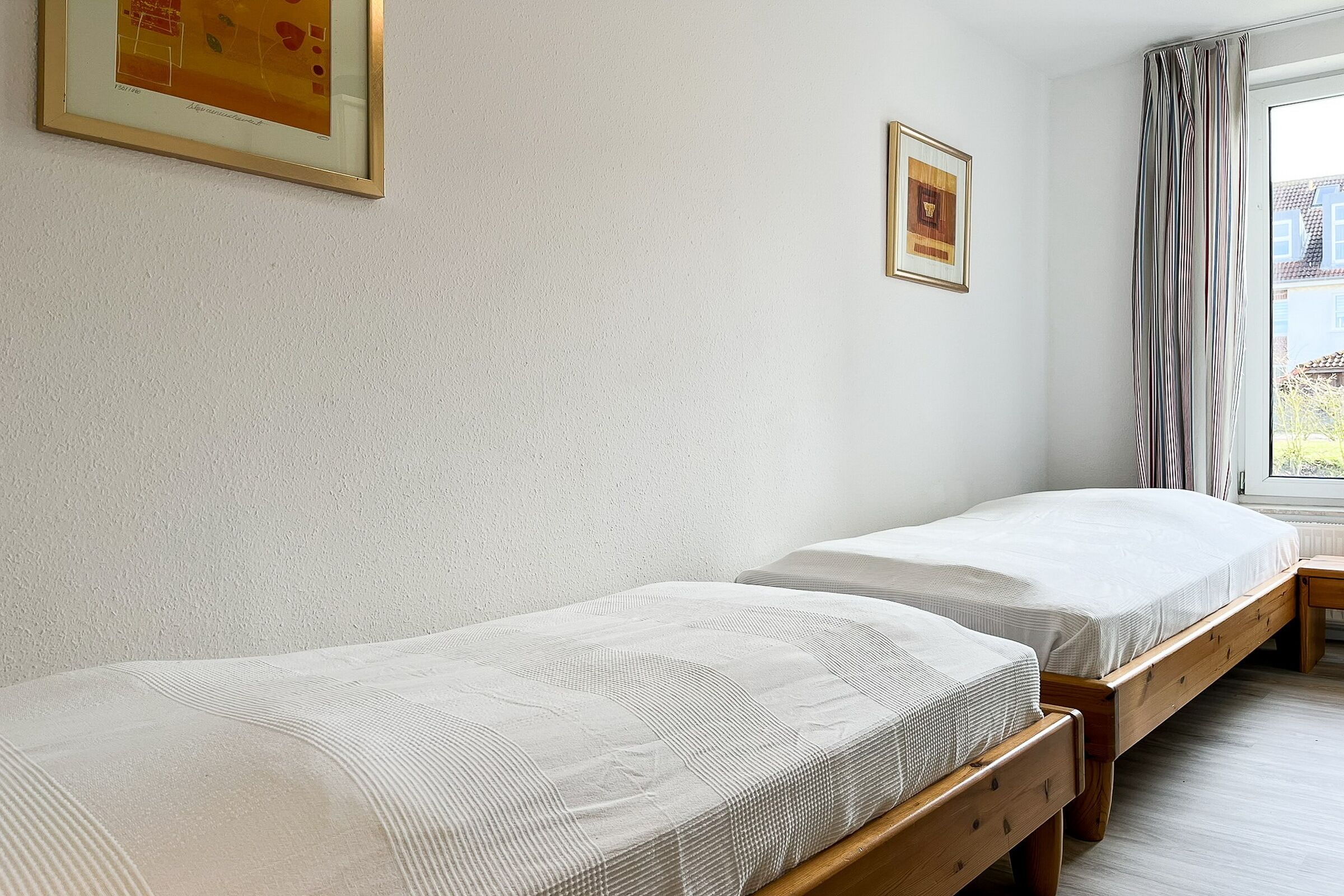 Una habitación con dos camas individuales, un banco de madera, un cuadro en la pared y una ventana con cortinas.