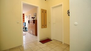 A hallway with a wooden door, a red doormat, and a light fixture.