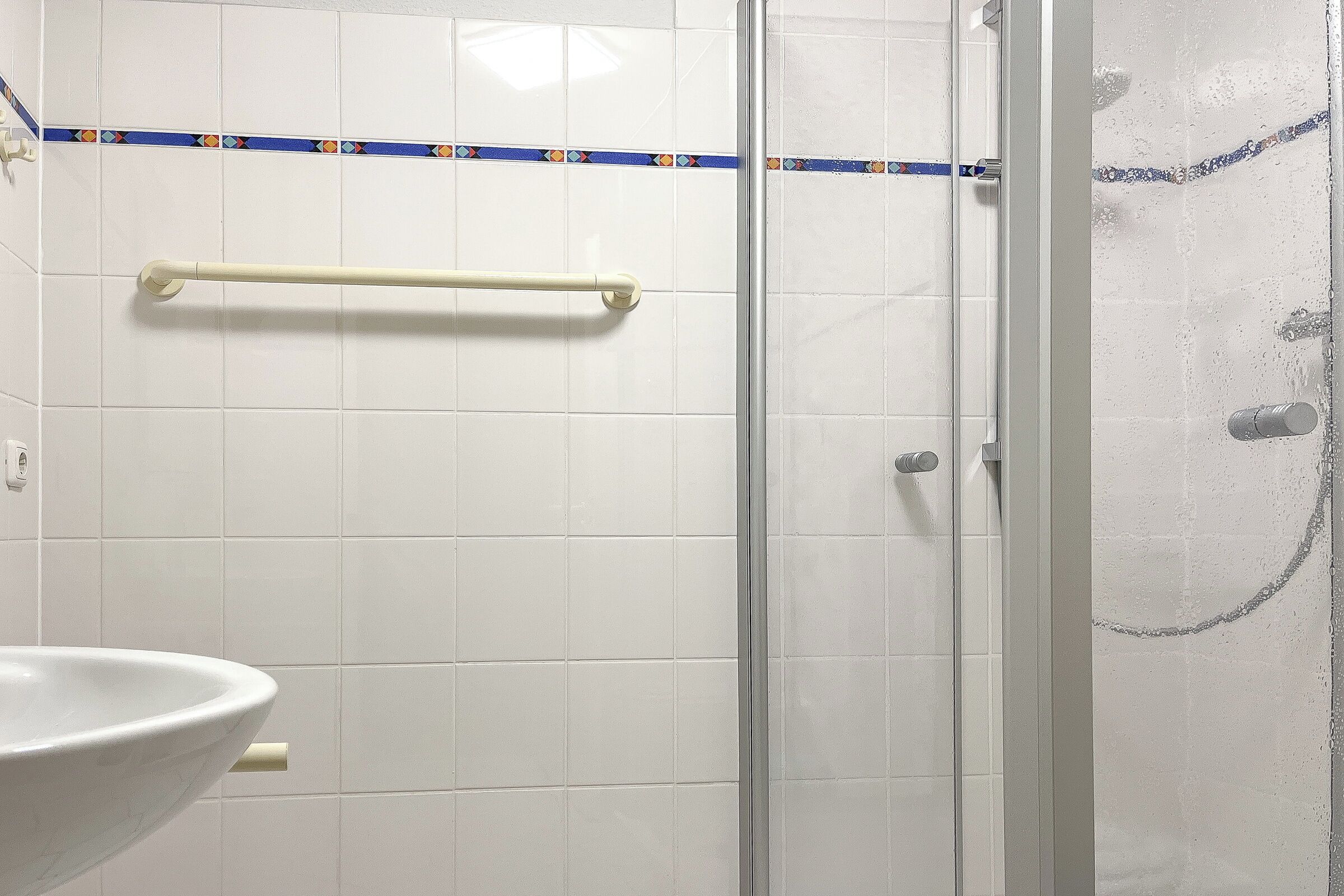 Een badkamer met een douchecabine van glas, een witte wastafel en een handdoekhouder.