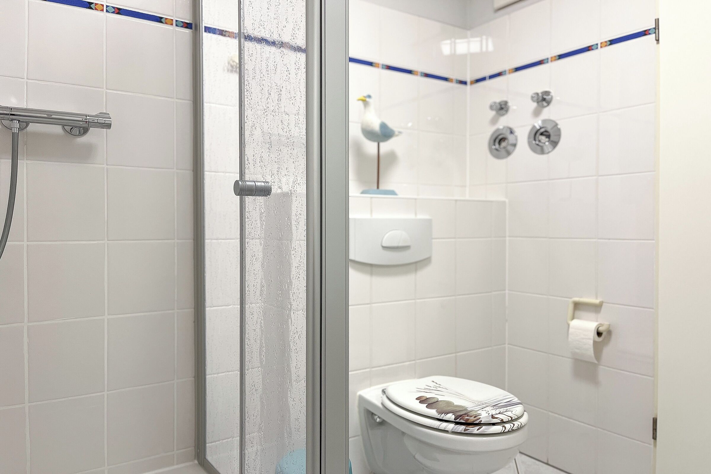 A bathroom with a shower, toilet, and a decorative bird on the wall.