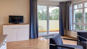 Et moderne værelse med et fjernsyn på et hvidt skab, en sofa og et stort vindue med gardiner.