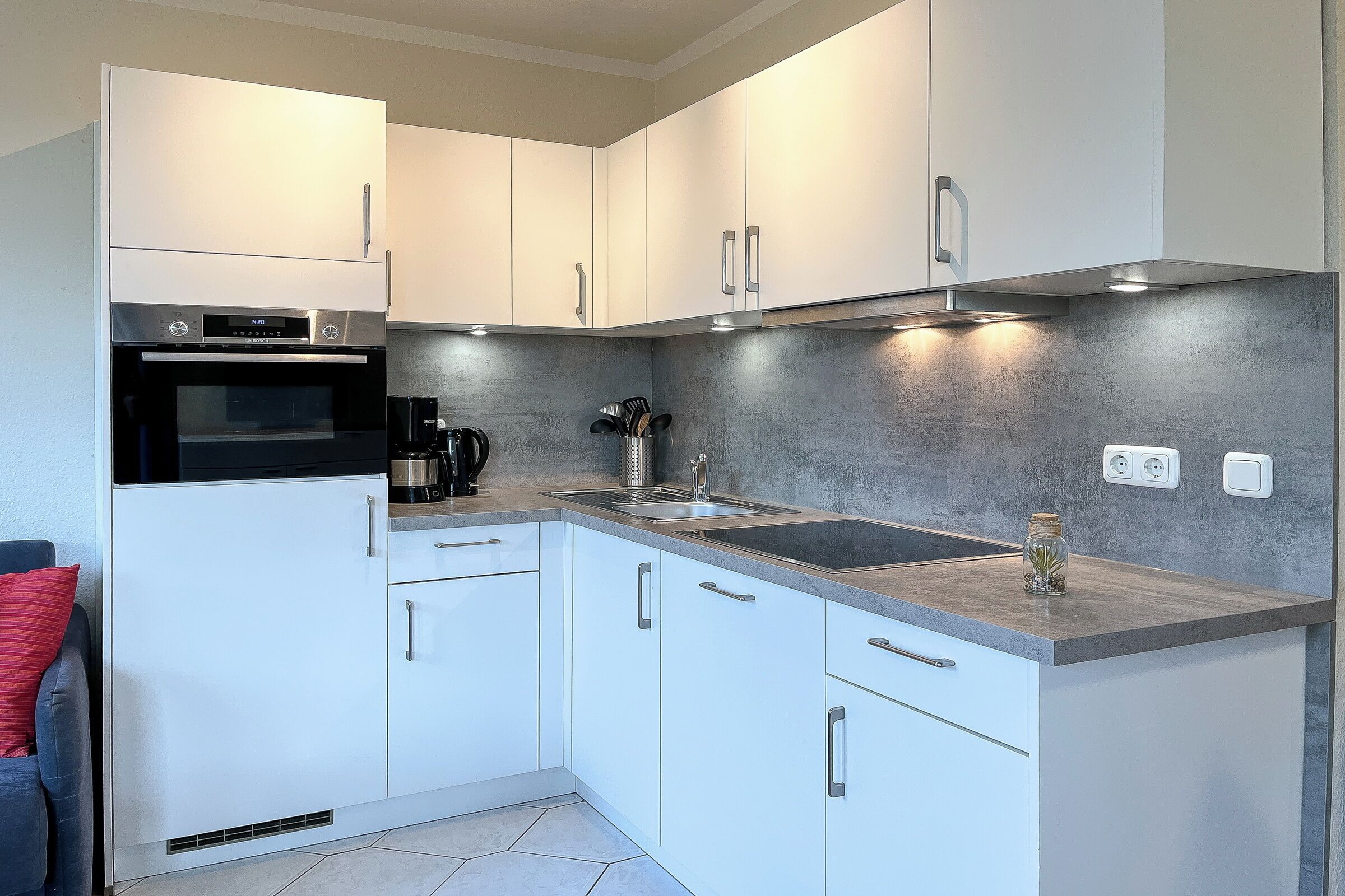 A modern kitchen with white cabinets, a built-in oven, a stainless steel range hood, and a grey countertop.