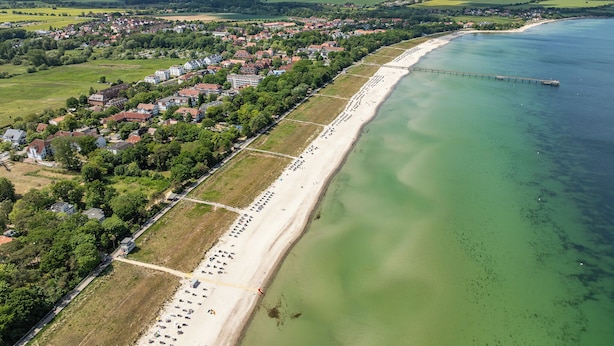 An aerial view of a coastal town with a long sandy beach, a pier extending into the water, and a mix of residential and commercial buildings. - Likedeeler Wohnung 06 (Ostseebad Boltenhagen)