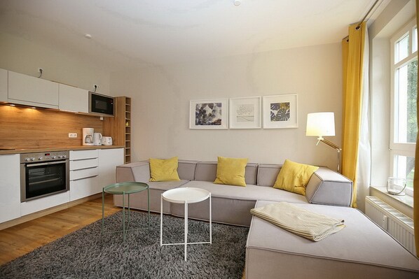 A modern living room with a sofa, a small round table, and a kitchen area with a microwave and oven.