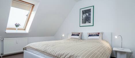 Une chambre à coucher avec un lit, une fenêtre, un tableau au mur et une table de chevet avec une lampe.