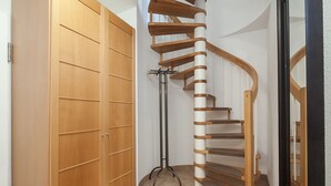Een hoek met een houten kast, een zwarte vloerlamp en een houten spiltrap.