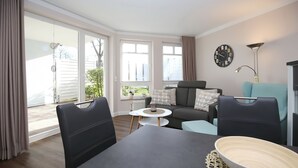 A modern living room with a dining table, two sofas, a small side table, and a large window with curtains. - Likedeeler Wohnung 08 (Ostseebad Boltenhagen)