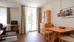 A spacious living area with a wooden dining table, chairs, a television, and a cabinet. - Sünnslag Wohnung 144 (Ostseebad Boltenhagen)