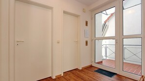 A hallway with wooden flooring, white doors, and a glass door leading to an outdoor balcony with a metal railing. - Sünnslag Wohnung 144 (Ostseebad Boltenhagen)