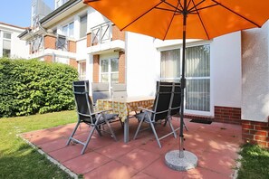 Un patio al aire libre con una mesa, sillas, un paraguas naranja y un seto.
