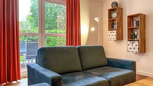 A living room with a sofa, a floor lamp, and a bookshelf with books and a clock. - Sünnslag Wohnung 131 (Ostseebad Boltenhagen)