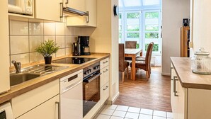 A modern kitchen with a built-in oven, a coffee machine, and a dining area with a table and chairs. - Sünnslag Wohnung 131 (Ostseebad Boltenhagen)
