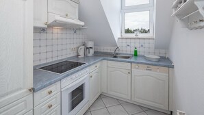 Una cocina con armarios blancos, horno empotrado, cafetera y ventana con vistas a árboles.