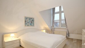 Un dormitorio con cama, mesitas de noche, una ventana y un radiador.