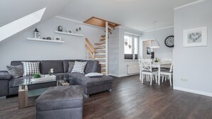 En moderne stue med en grå hjørnesofa, et glasbord og en trætrappe.