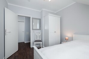 Une chambre à coucher comprenant un lit, une armoire, une chaise et une table de chevet avec une lampe.