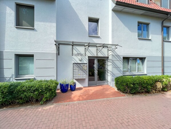 Un edificio moderno con fachada plana, una entrada central con puerta de vidrio y una pequeña señal encima de la puerta.