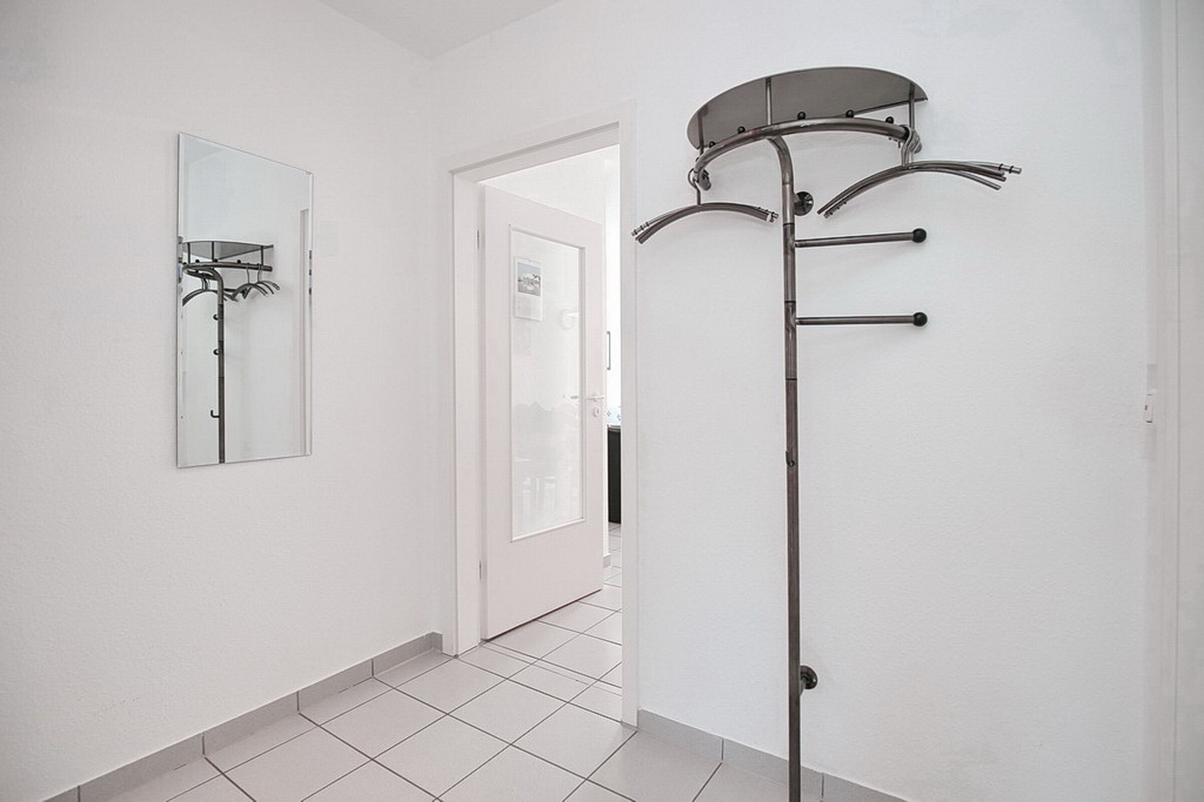 Un couloir avec un porte-manteau, un miroir et une porte donnant sur une autre pièce.
