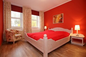 Ein Schlafzimmer mit einem hölzernen Bett, floralen Vorhängen, einem Nachttisch mit Lampe und einem Bild an der Wand.