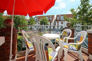 Eine Terrasse mit weißen Plastikstühlen und einem roten Sonnenschirm, mit Blick auf ein Wohngebiet mit Häusern und Grünflächen.