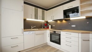 A modern kitchen with white cabinetry, a built-in oven, and a microwave. - Sünnslag Wohnung 122 (Ostseebad Boltenhagen)