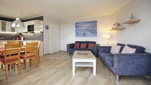 A modern living room with a dining area, a sofa, a coffee table, and a kitchen in the background. - Sünnslag Wohnung 122 (Ostseebad Boltenhagen)