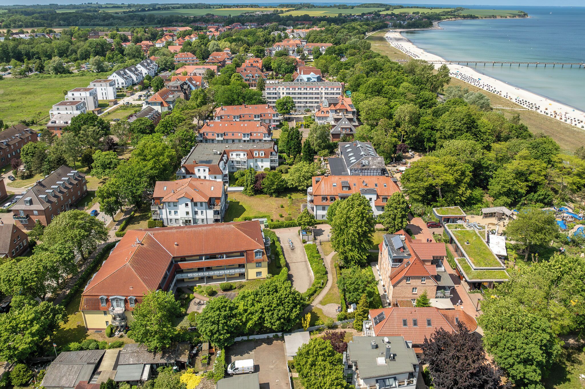Oversigtsbillede af et kystnært boligområde med huse, en strand og en mole.